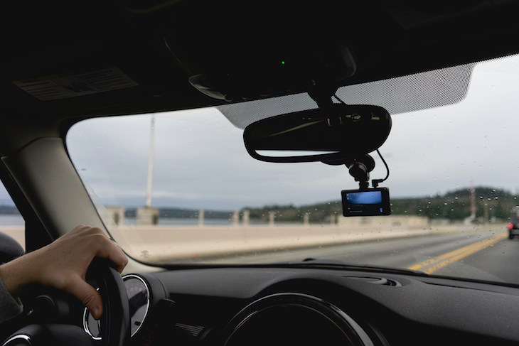 photo showing windshield of car from the backseat with a dash cam attached to the rearview mirror