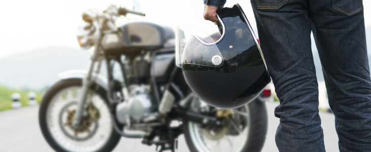 Person holding a helmet standing near a parked motorcycle on a road in North Dakota, related to personal injury attorney