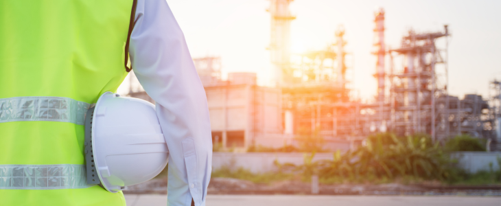 Worker in a high-visibility vest holding a hard hat, standing in front of an industrial plant at sunset in North Dakota, related to personal injury attorney