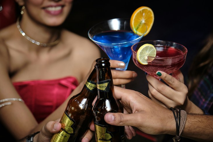 group of individuals raise glasses and beer bottles in a celebratory cheers