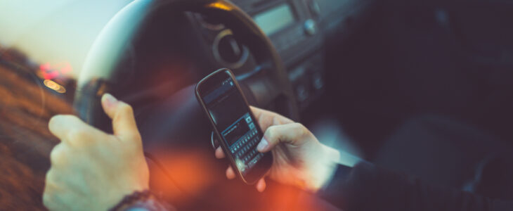 Young businessman driving a car and using smartphone