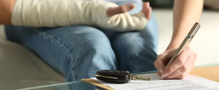 Close up of a lady hands with broken arm signing insurance document after car accident at home